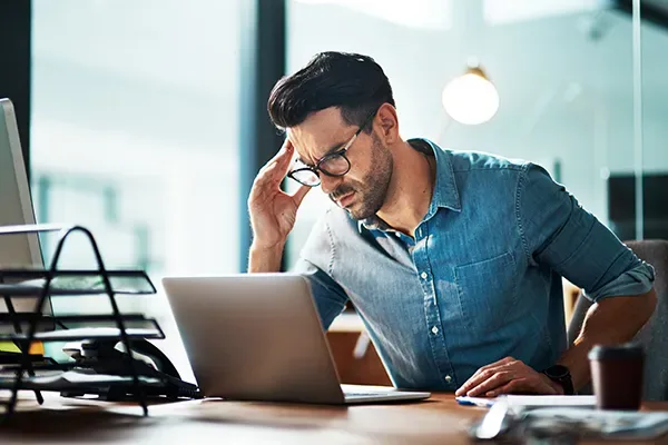 Funcionário preocupado, com a mão na cabeça, diante do notebook em um escritório